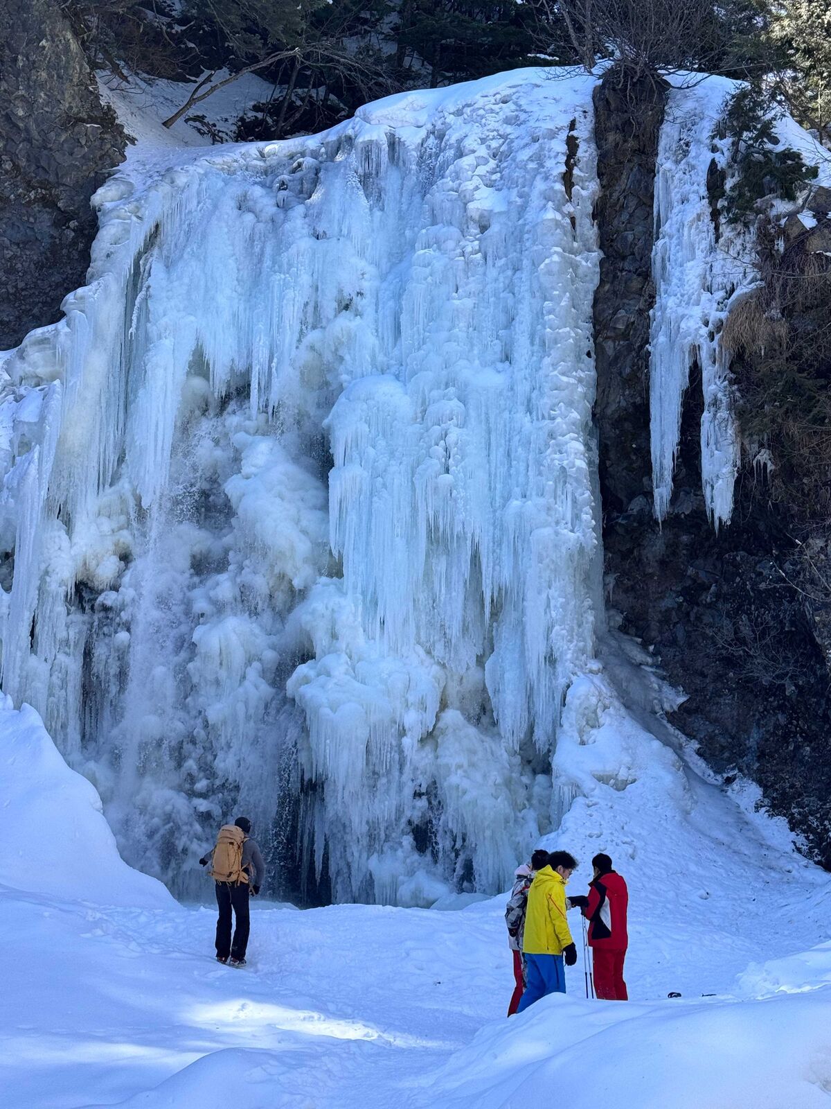 巨大な氷柱に覆われた氷瀑を見上げるスノーシュー客たち
