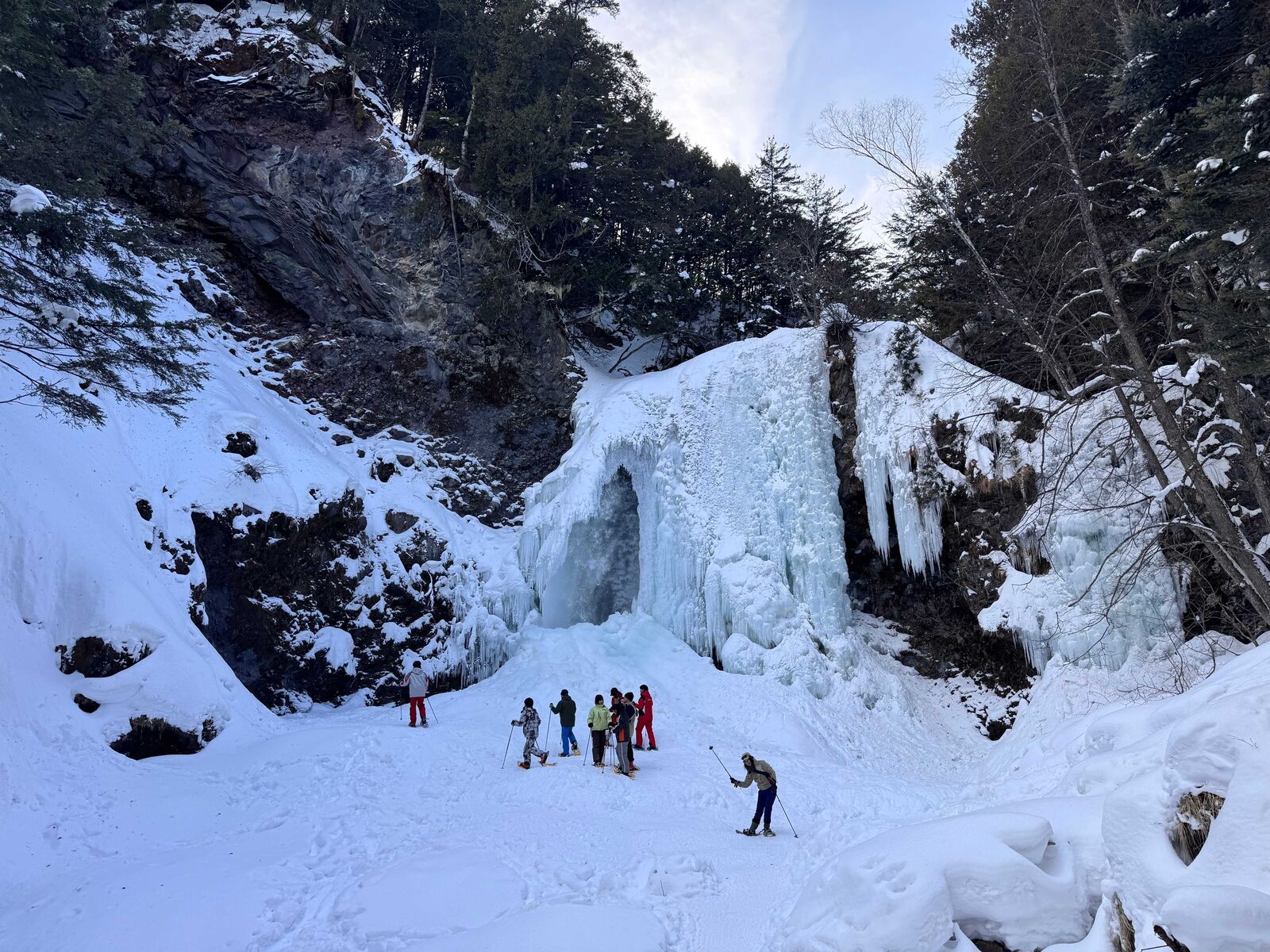 森の中に現れる、青白く輝く氷瀑と雪原を進むスノーシューツアーの一行