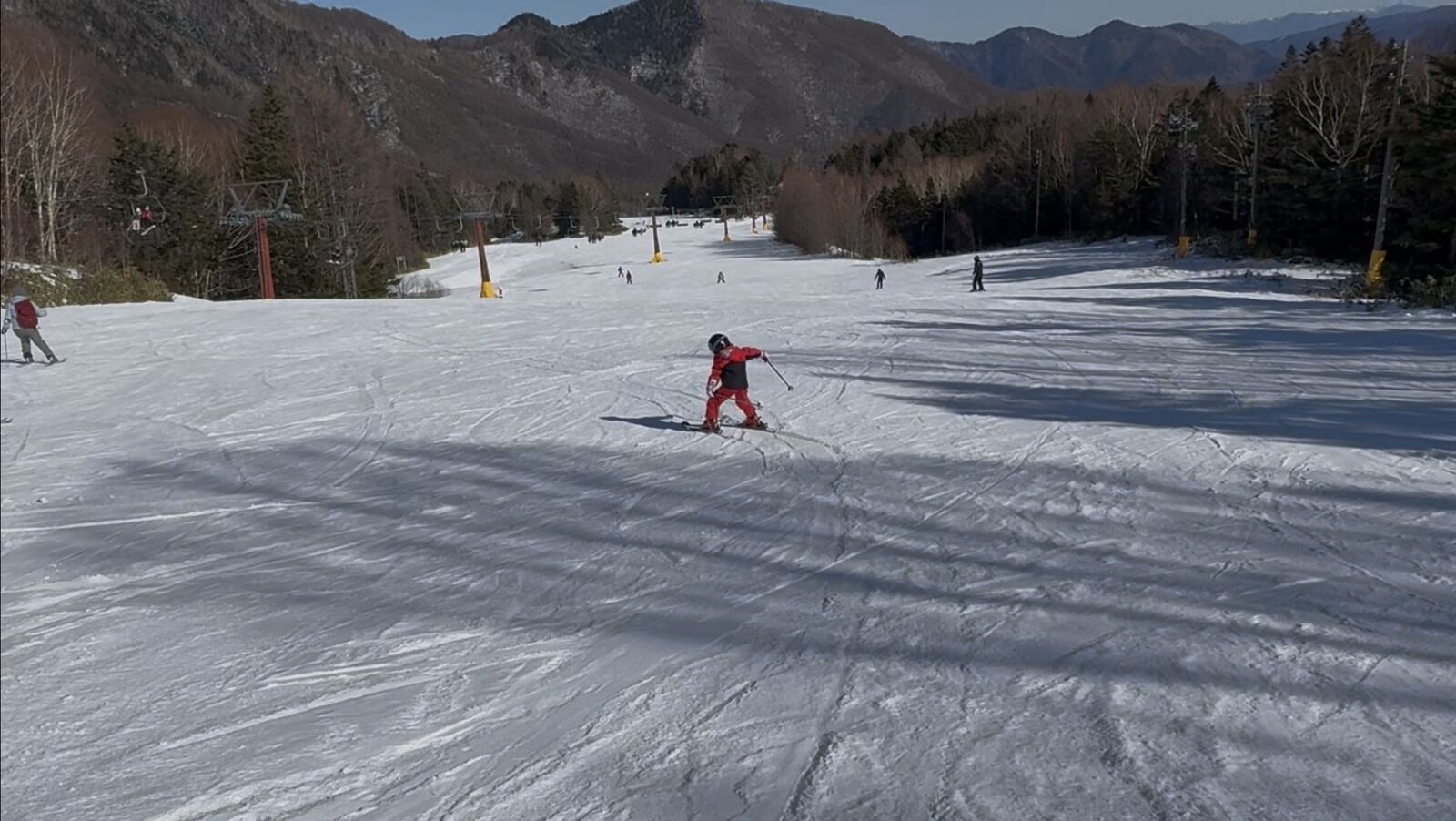夢の平コースを滑るスキーヤーと、なだらかに広がるゲレンデ、奥に見えるリフト